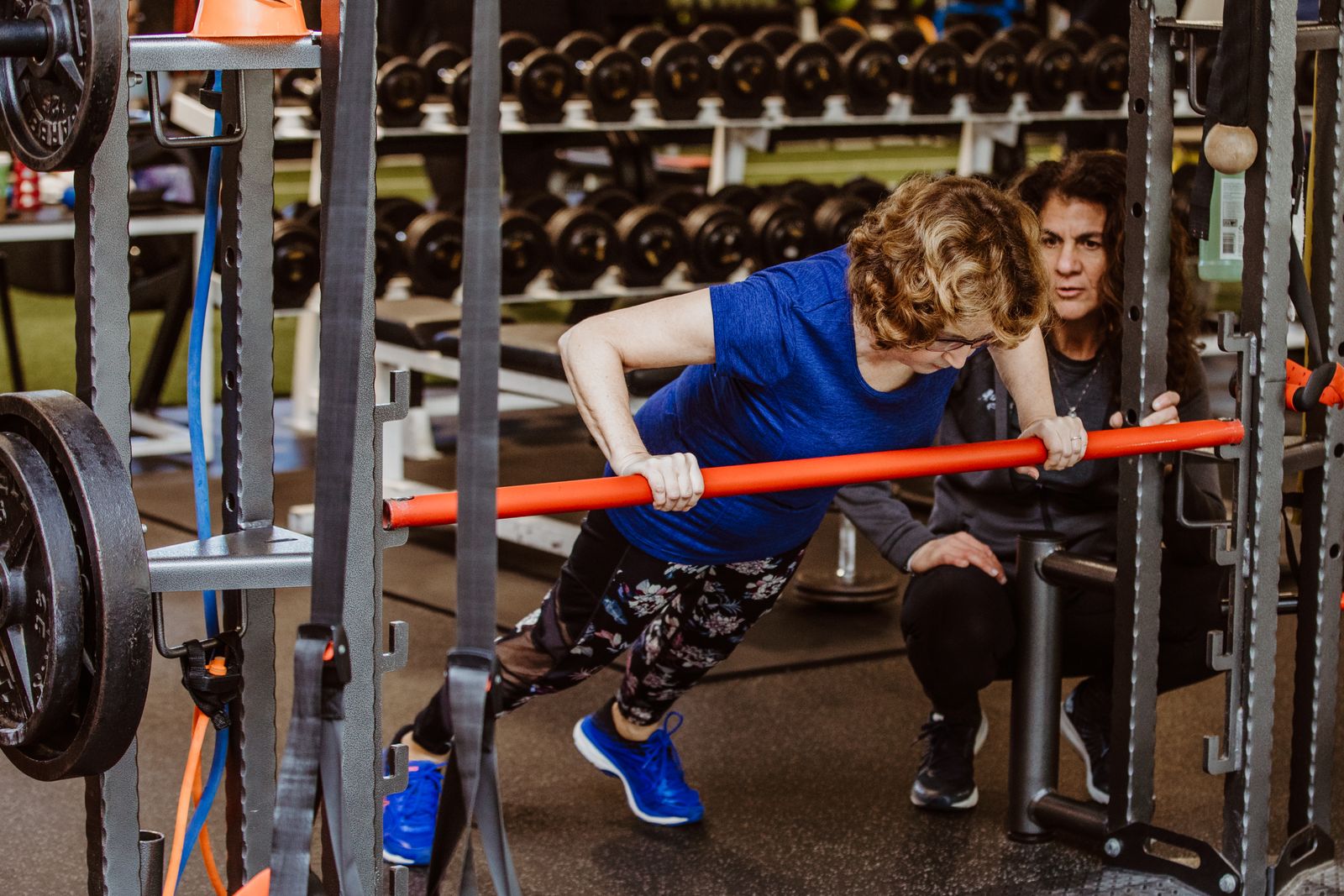 A coach cues a member through incline push-ups on a barbell