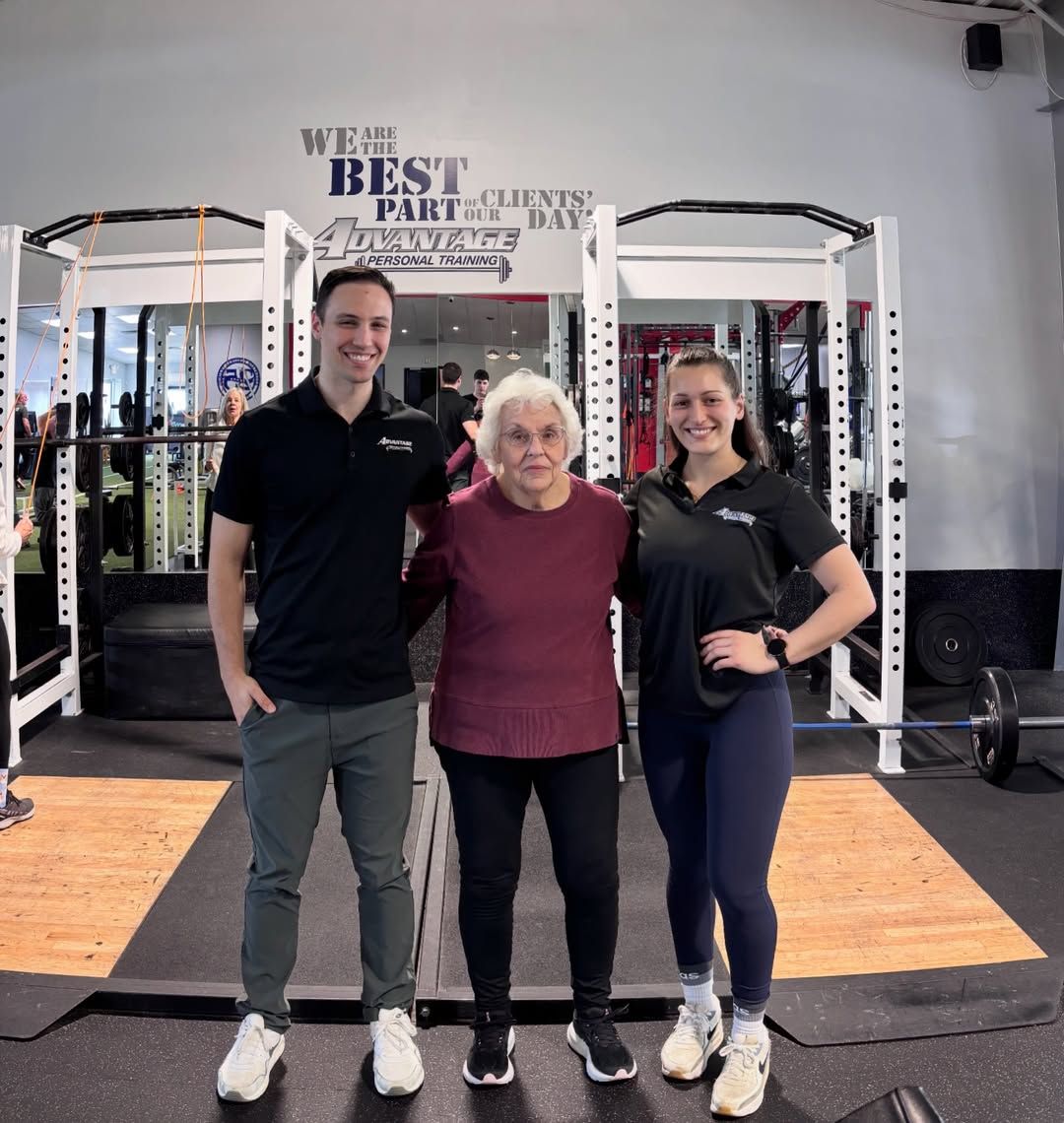 Two Advantage coaches with an older member under the gym’s wall decal