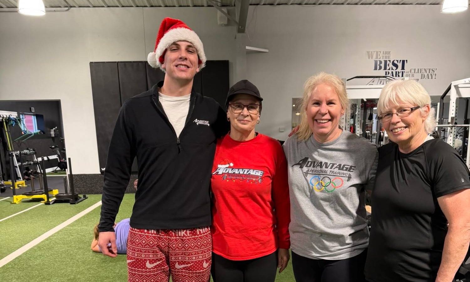 A coach in a Santa hat with three members in Advantage shirts, smiling together on the turf at the gym