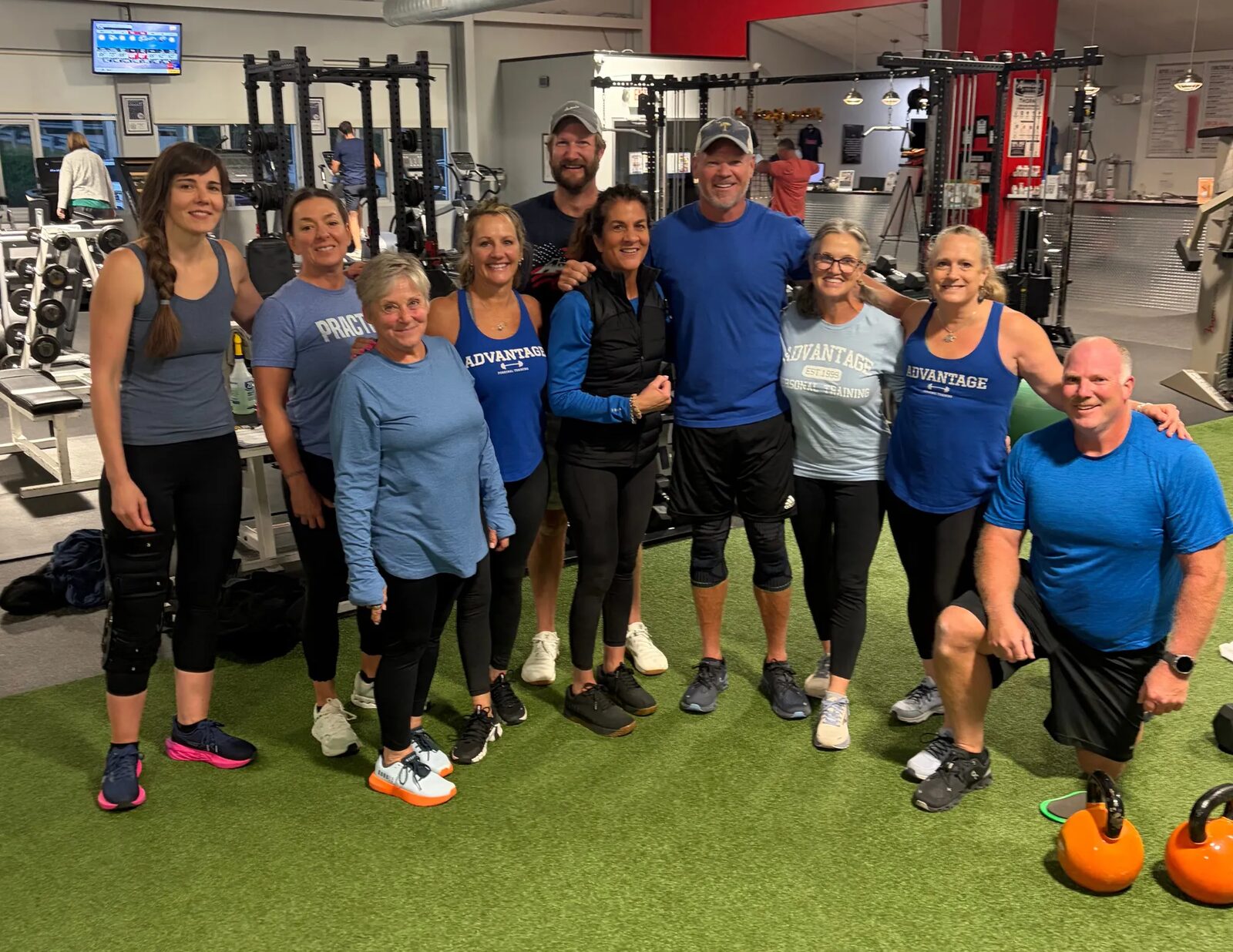 A group of Advantage members and coaches smiling together on the turf at the gym