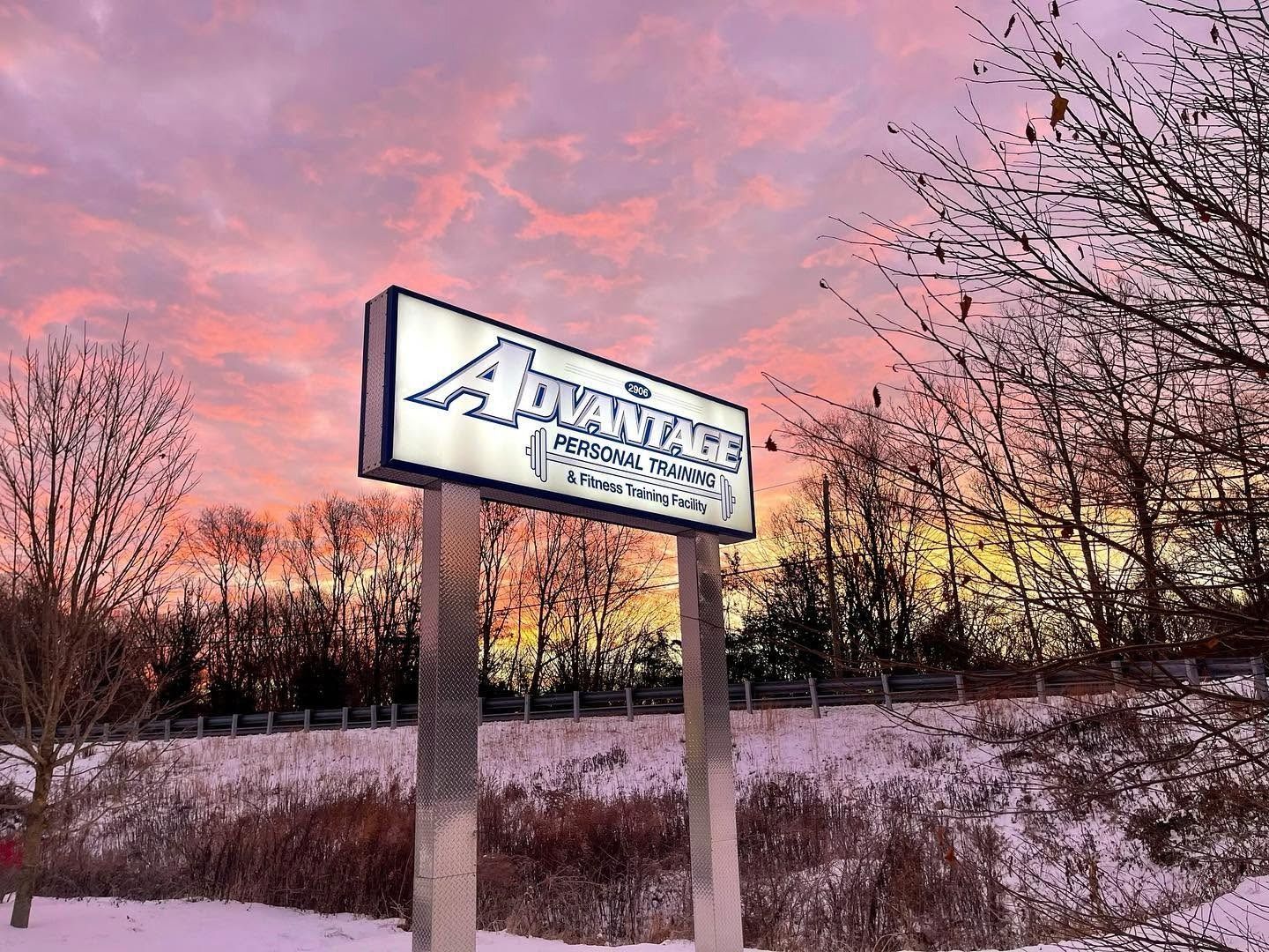 The Mystic gym’s lit Advantage Personal Training roadside sign at sunset, snow on the ground