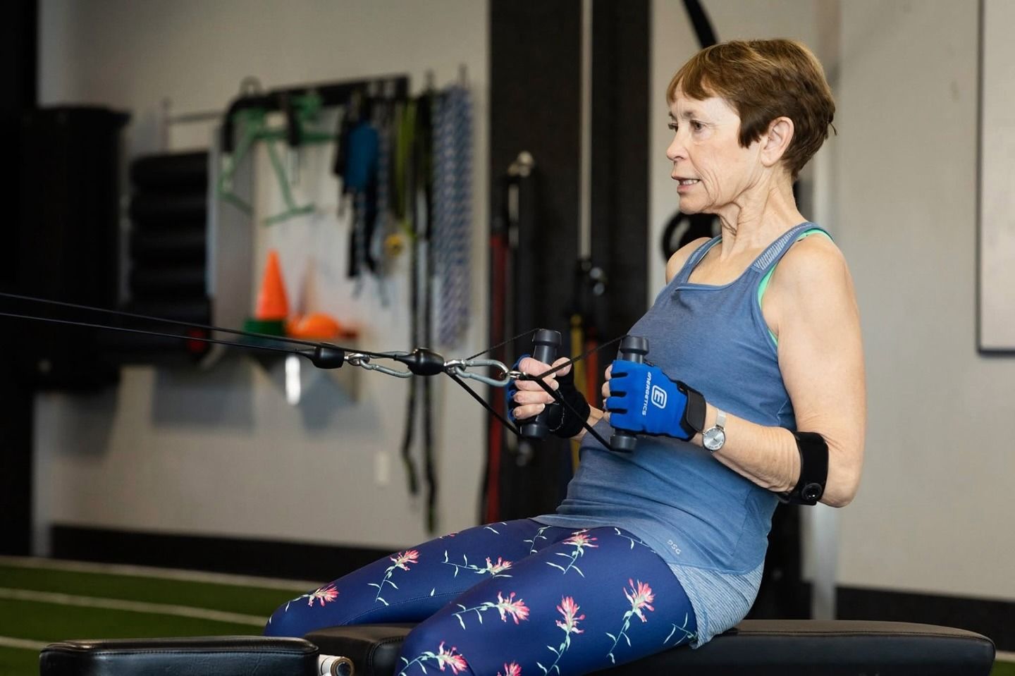 An older member in training gloves pulls a seated cable row, focused.