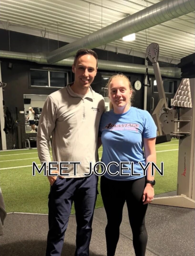 Jocelyn in a blue Advantage T-shirt standing beside her coach, Adam, on the gym’s turf